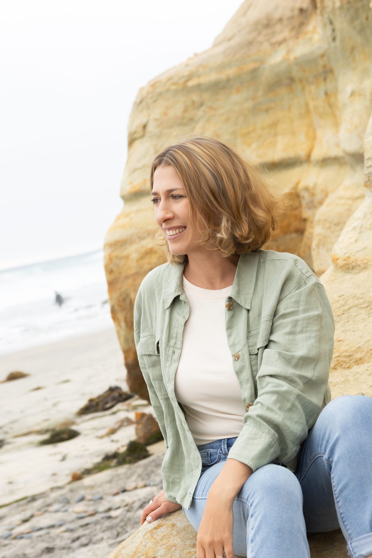 Vera McGrath, Licensed Marriage and Family Therapist, seated on rocks by the coast