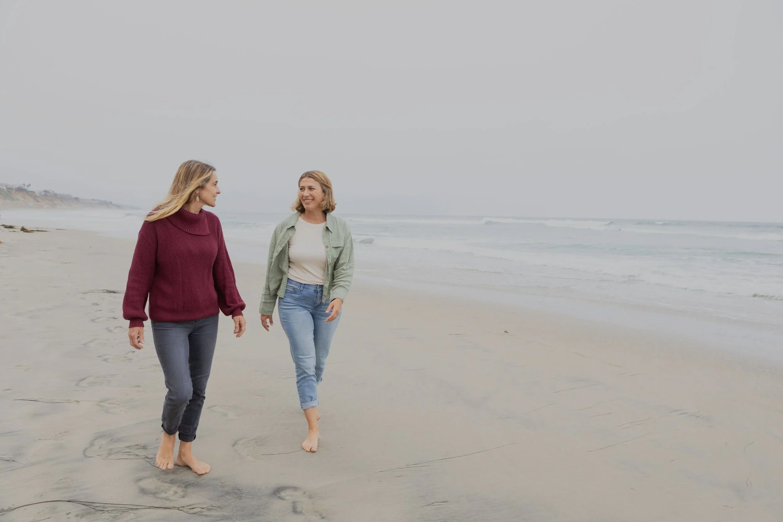 Two friends walking side by side along the beach, talking as they go